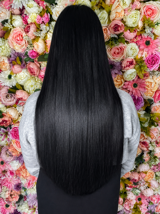 Long black hair extensions styled straight against a floral wall 